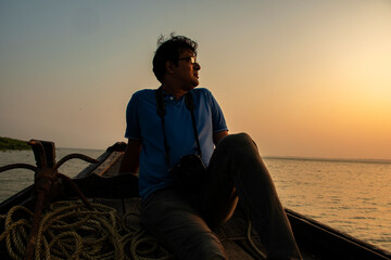 Fototapeta premium An young solo traveler sitting on the adge of a country boat looking at the mangrove forest of Sundarban Tiger Reserve.