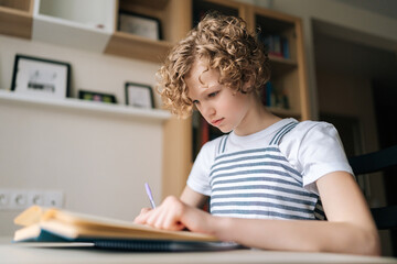 Low-angle view of concentrated little child schoolgirl writing in exercise book doing some...