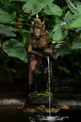 Fließendes Wasser von der Buddha-Statue im Hintergrund der grünen Blätter