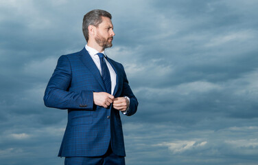 Professional man sky background. Grizzled man buttoning suit. Serious man looking aside, copy space