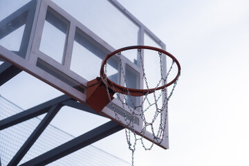 outdoor basketball in front of a blue sky. The basketball hoop or ring is orange and its pole is...