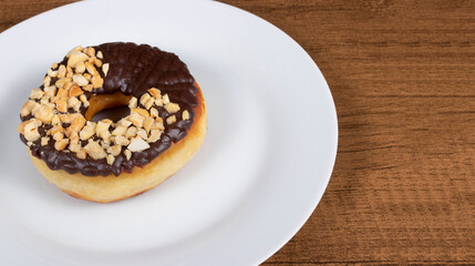 Sweet donuts with chocolate icing and walnuts served on a white plate. Close-up photography with elements on the left with empty space for texts on the right.