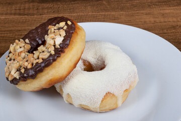 Sweet donuts with cream and powdered milk frosting and another donuts with chocolate and chestnut frosting and nuts served on a plate.