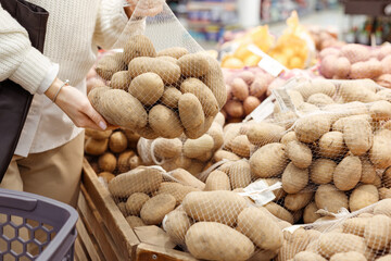Woman buying mesh bag with potato in supermarket or farm market, vegetables