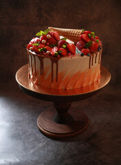 Beautiful delicious dessert cake with strawberries, mint and waffle doused with chocolate on a wooden stand in a dark background