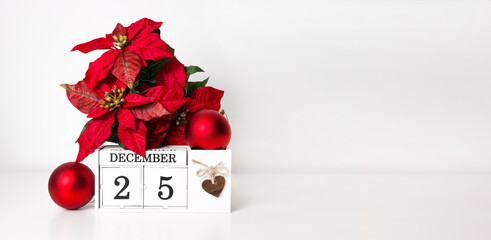 White wooden calendar near christmas ornaments and poinsettia. Holidays banner with place for text
