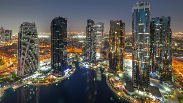 Tall residential buildings at JLT district aerial day to night transition panoramic timelapse, part of the Dubai multi commodities centre mixed-use district. Villa houses on a background