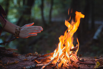 Close up hands warming over campfire concept photo. Make fire in forest. Side view photography with woman hands on background. High quality picture for wallpaper, travel blog, magazine, article