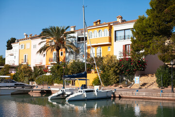 Obraz premium Colorful yellow houses, yachts and palm trees in Port Saplaya, Valencia, Spain on a sunny day landscape. Street and canal with boat in Europe. Travel destination for relaxing vacation.