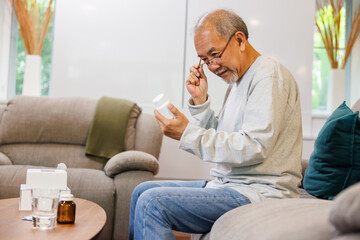 Senior Asian man taking prescription medicine at home. older man reading drug label with...
