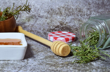 Honey and herbs from the woody stems of rosemary, on a stone background, along with a glass jar and...