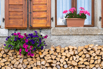 Beautiful cottage window decorated with chopped woods and flowers in a small village in alps, Sauris, Italy
