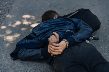 The detained criminal lies on the ground face down, hands behind his back in handcuffs.