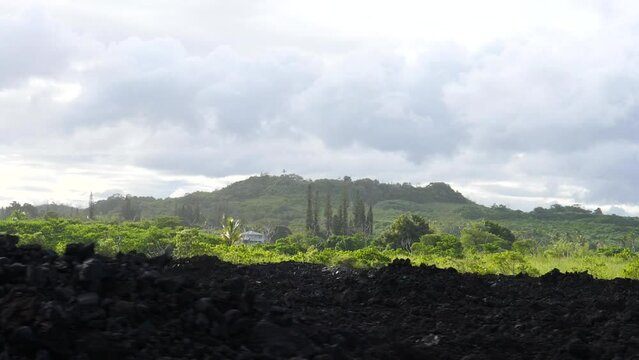 Wide establishing shot of Hawaii Big Island with hardened lava rock and green forested jungle on an overcast but sunny day
