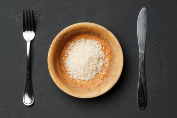 Heap of dry rice in a bowl on black background, lack of food, hunger concept