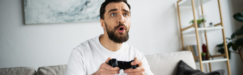 Obraz premium KYIV, UKRAINE - OCTOBER 21, 2022: tensed and bearded man holding joystick and playing video game, banner.