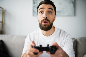 KYIV, UKRAINE - OCTOBER 21, 2022: focused and bearded man holding joystick and playing video game.