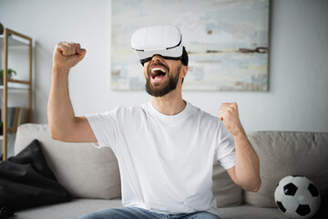 amazed and bearded man in vr headset rejoicing while gaming in living room.