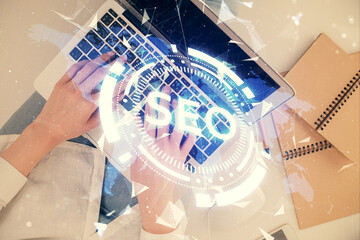Double exposure of woman hands working on computer and SEO hologram drawing. Top View. Search optimization concept.