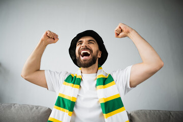 excited man in fan hat and stiped scarf celebrating while watching championship.