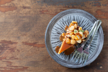 A tabletop view, flat layout with copy space of a single piece of tasty caramel sauce macadamia nut cheesecake on a small rounded plate and forks on old wooden table. Cafe, Bakery, pastry concept.