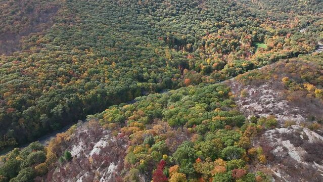 An aerial view high above the mountains in upstate NY in the fall on a sunny day. The camera dolly in tilted down and passes over a road high up in the mountain top.