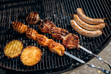 tasty appetizing grilled sausages, fried pineapples, barbecue meat on a metal grill, cooked outdoors - 546546097