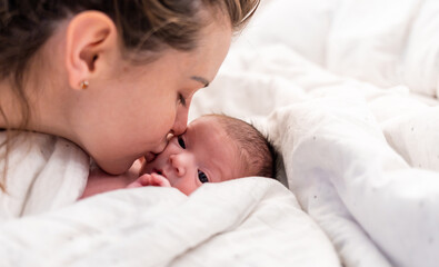 Obraz na płótnie Canvas Loving mom kissing her newborn baby child lying in bed