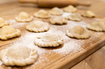 Raw dumplings polish traditional perogies lying on wooden board in kitchen