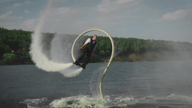 An office clerk flies a flyboard after a day's work. A man performs dangerous and extreme stunts over water