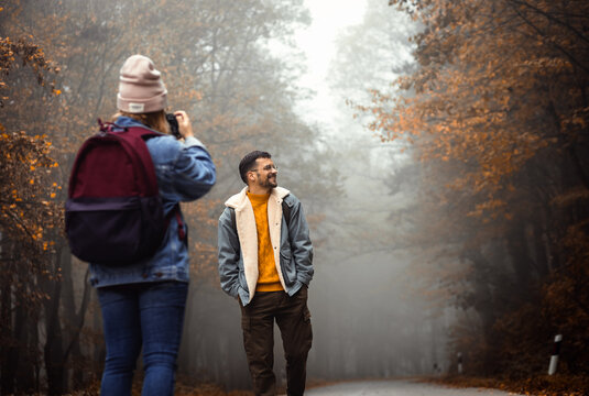 Couple spending time together walking on forest road on photographing each other a foggy morning.