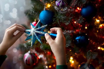 The hands of a child decorating an artificial Christmas tree with a blue star. The atmosphere of preparation for the holiday. The dark key. Zero waste