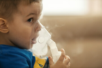 Profile of a little boy making inhalation with nebulizer at home.