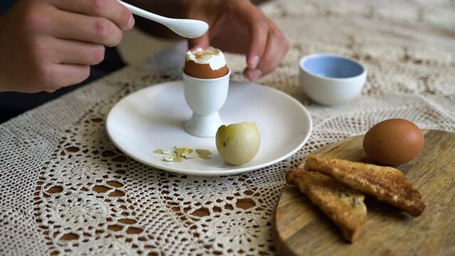 Close up of eating tasty boiled egg in a cup with spoon for breakfast. Healthy meal on the kitchen table.