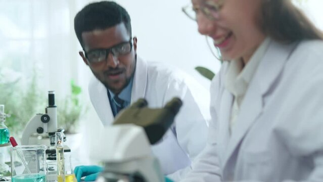 Young caucasian Female Microbiologist Talks to a african Male Biochemist about New Test Results.Bright Medical Science Laboratory with Diverse Team of Research Scientists Working.