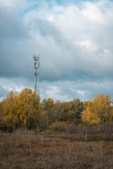 A metal radio tower towers over the autumn yellow trees. Blue sky. Autumn landscape. Beautiful shot of autumn forest and the broadcast antenna at the top of the hill during peak fall colors.