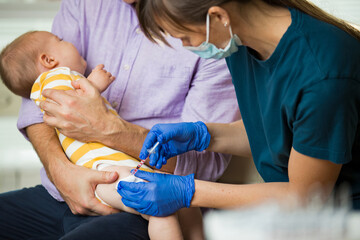 Female nurse with surgical mask and in gloves giving vaccine injection to a baby in clinic. Infant...