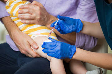 Female nurse with surgical mask and in gloves giving vaccine injection to a baby in clinic. Infant...