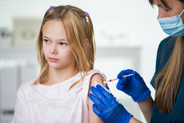 Female nurse with surgical mask and in gloves giving vaccine injection to a teenager in clinic....