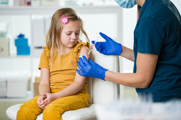 Female nurse with surgical mask and in gloves giving vaccine injection to a child in clinic....