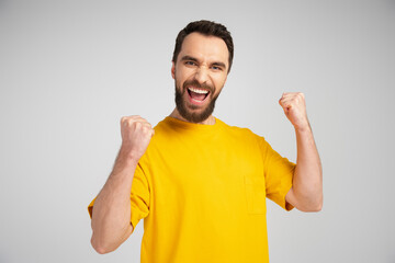 Fototapeta premium excited man in yellow t-shirt shouting and showing success gesture isolated on grey.