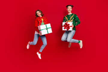 Full body photo of overjoyed energetic people jumping hands hold newyear festive giftbox isolated on red color background
