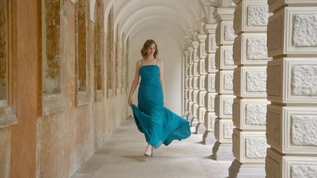 A beautiful blonde woman walks elegantly in a graceful blue dress.