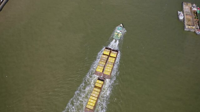 Thames river traffic, Cory tug towing barges of lemon-yellow containers, top-down aerial view.