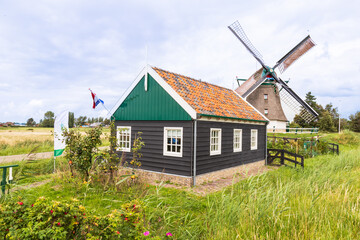 Wooden shop with Dutch flag and a corn mill in the background in the rural village of Akersloot.