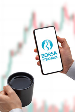 İstanbul, Turkey - Nov 16, 2022: A Smartphone With The Borsa Istanbul Logo In Hand. Borsa Istanbul Stock Chart On The Background.