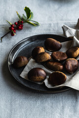 Step by step process of making roasted chestnuts. Raw chestnuts on linen napkin on dark plate.