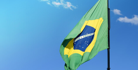 Brazilian flag waving in a beautiful blue sky day, with the sunlight lighting up the flag. Brazil flag on the right with space for text on the left.