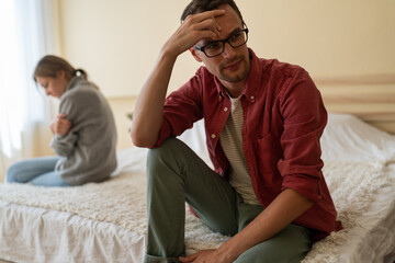 Obraz premium Young unhappy European family couple sitting separately on bed at home, thinking of breakup, having problems in relationship. Man and woman in love feeling sad and depressed after fight