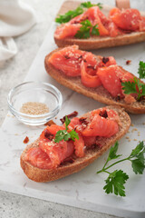 Sandwiches with salted salmon. Open sandwiches from cereal or whole grain rye bread with salted salmon, sesame seeds and dried tomato on white marble stand. Seafood. Healthy food. Scandinavian cuisine